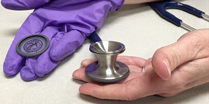 Mains tenant la tête de stéthoscope 3M ™ Littmann® ClassicIII ™.
