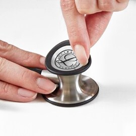 Doigts retirant la membrane double fréquence de la cloche d’un stéthoscope 3M Littmann Classic III.